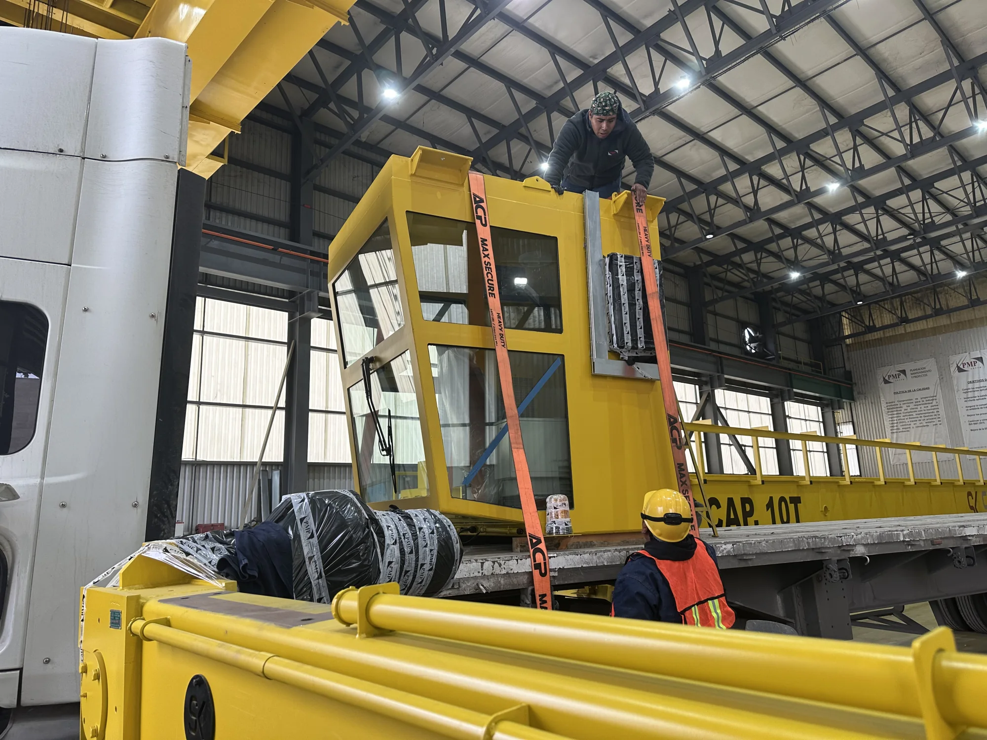Trabajadores asegurando una cabina amarilla de operación Strong Kranes durante una maniobra de montaje en taller