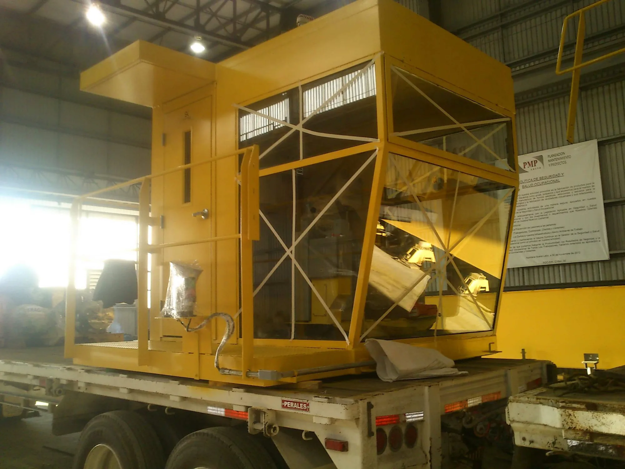 Cabina amarilla de operación industrial transportada sobre una plataforma dentro de un taller