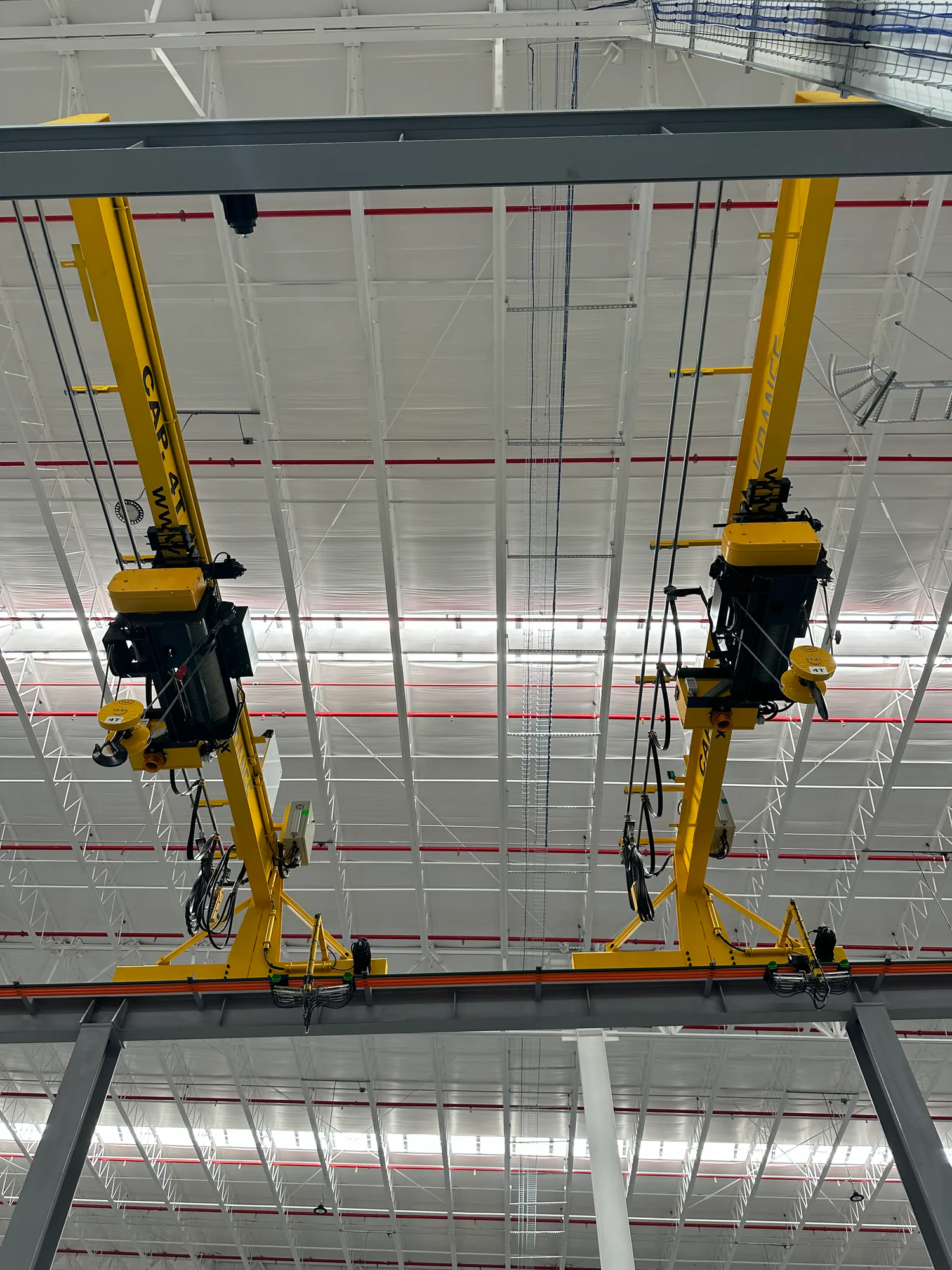 Vista inferior de dos grúas viajeras monopuente con polipastos instaladas en una nave industrial