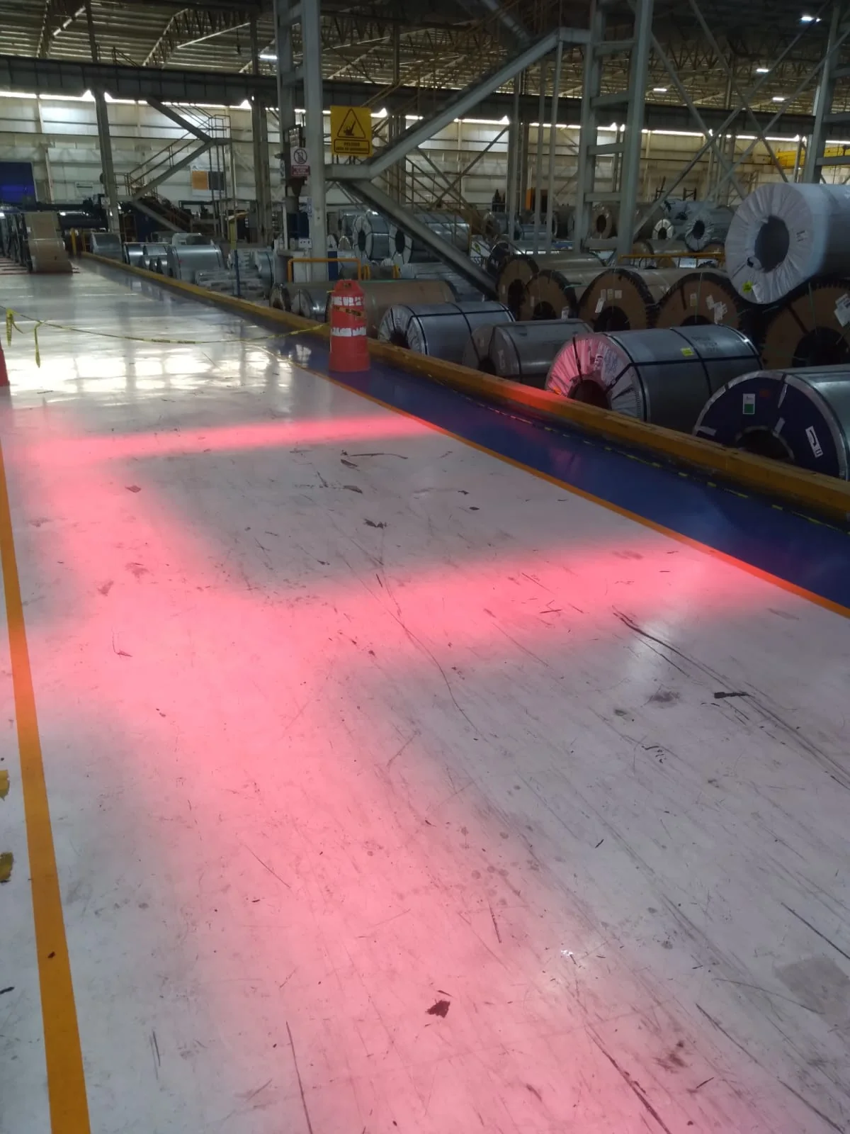 Proyección lineal roja de seguridad sobre el piso de un área industrial con bobinas de acero